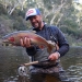A man is standing in the Thredbo River holding a rainbow trout in Kosciuszko National Park.